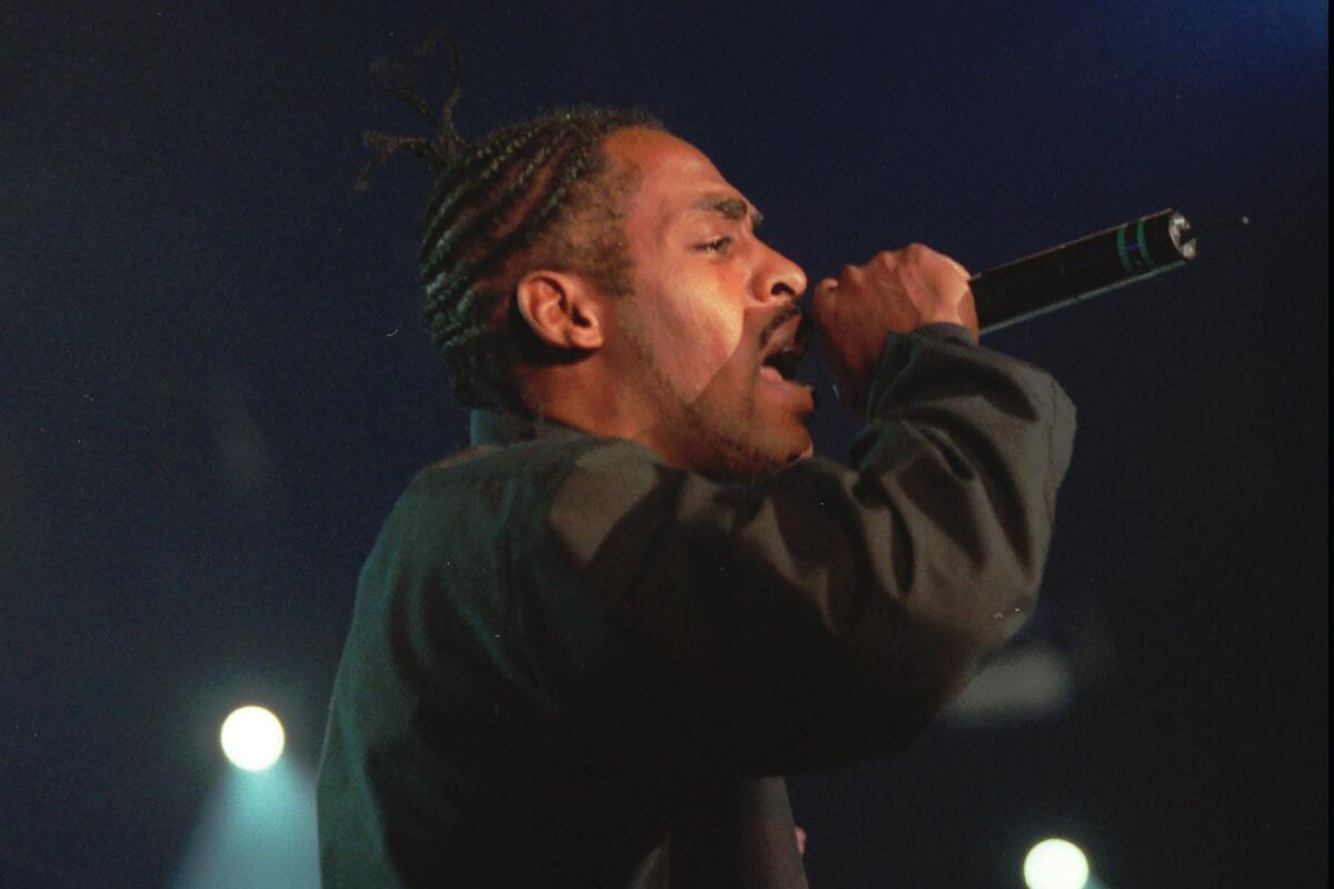 Coolio wearing a black jacket and holding a microphone to his mouth