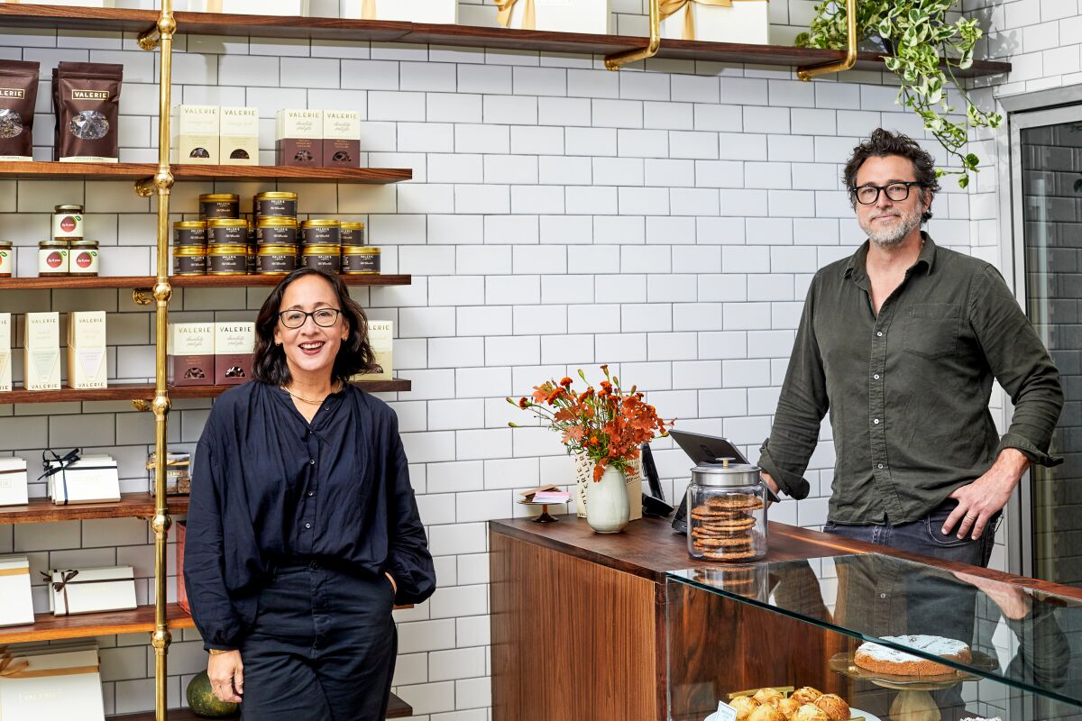 Gordon and Weightman Jr. stand in a white-tiled retail space. On the wooden shelves are jars of jams and chocolate bars.