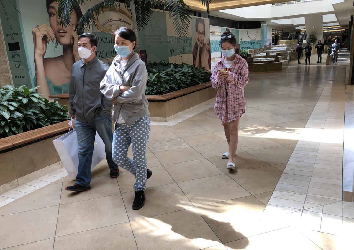 Shoppers wear face masks as they walk through the mostly empty South Coast Plaza in Costa Mesa on Monday, before the mall announced it was shutting down for two weeks because of COVID-19 concerns.