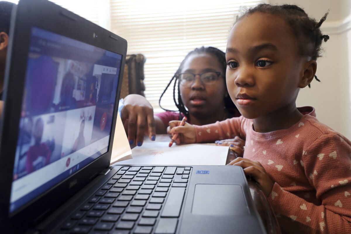 FILE — Lear Preston, 4, who attends Scott Joplin Elementary School, participates in her virtual classes as her mother, Brittany Preston, background, assists at their residence in Chicago's South Side, Feb. 10, 2021. Schools across America are racing to make up for lost classroom time, budgeting billions of dollars for tutoring, summer camps and longer school days. But figuring out which students need help has become its own challenge after the pandemic left holes in some students' learning records. (AP Photo/Shafkat Anowar, File)