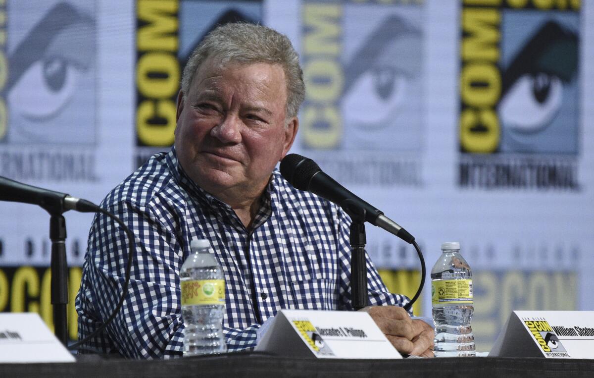 William Shatner wearing plaid shirt and sitting at a mic.