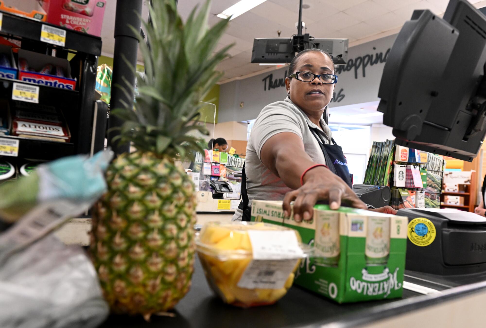 A supermarket cashier reaches for groceries on a conveyor belt.