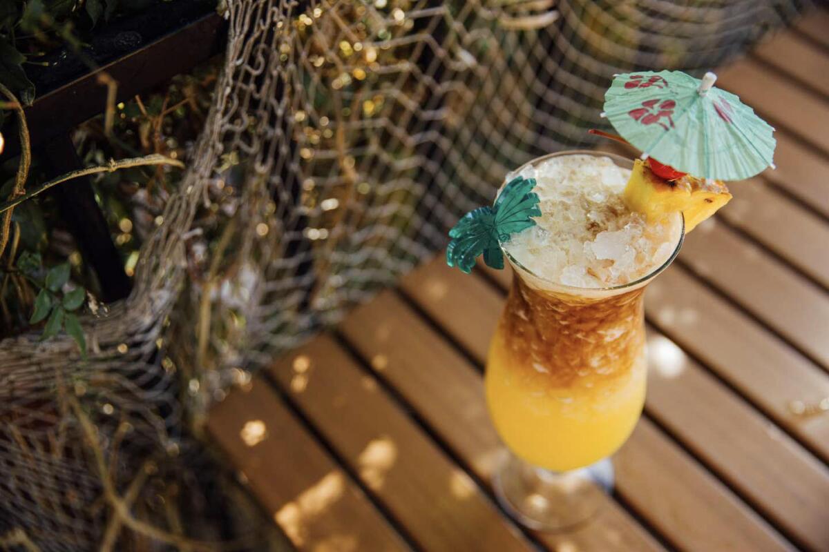 An overhead shot of a tropical cocktail on a wood table, with netting in the background.