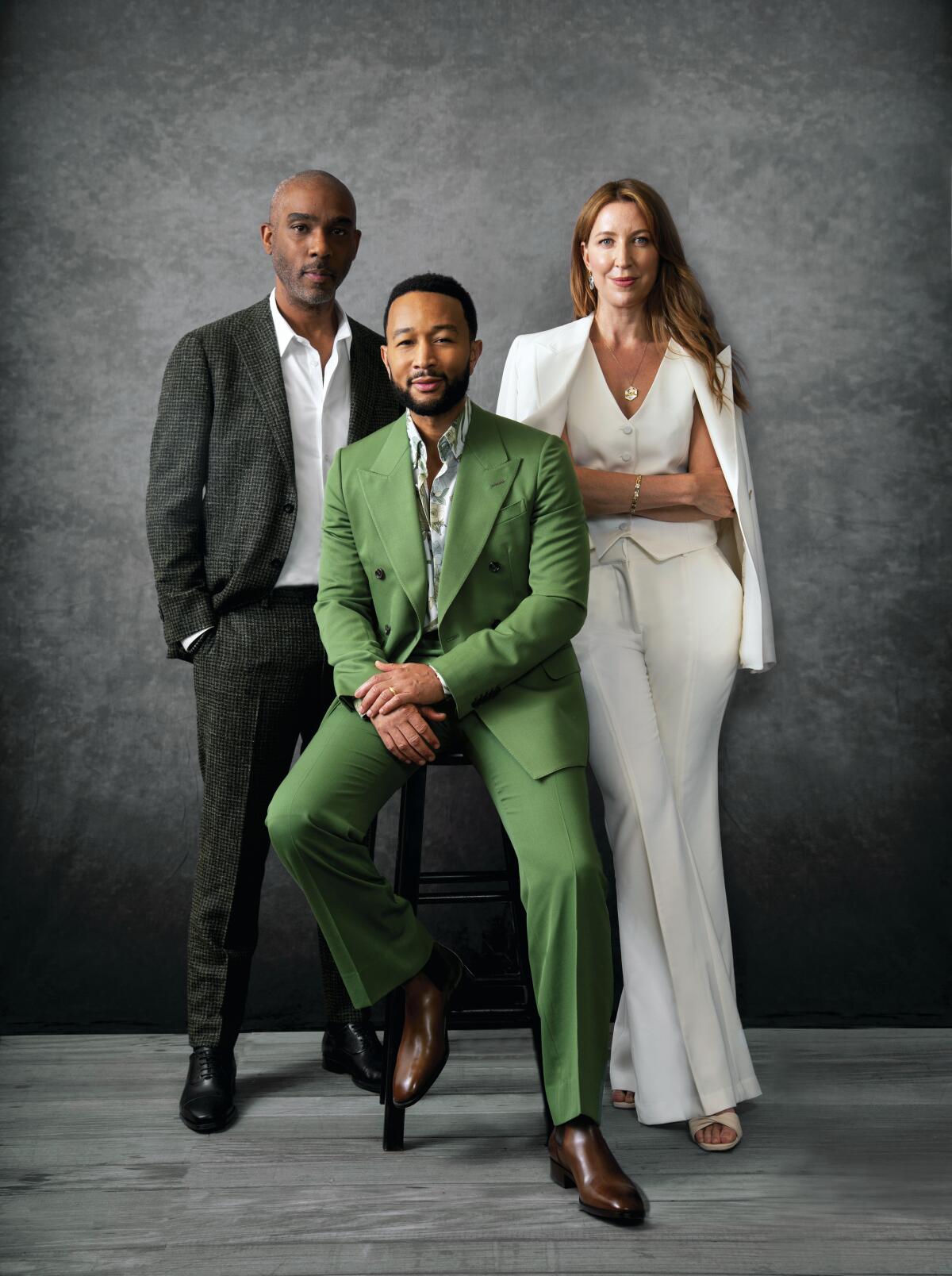 John Legend, in a green suit, sits on a stool while Mike Jackson and Ty Stiklorius, in a white suit, stand behind him.