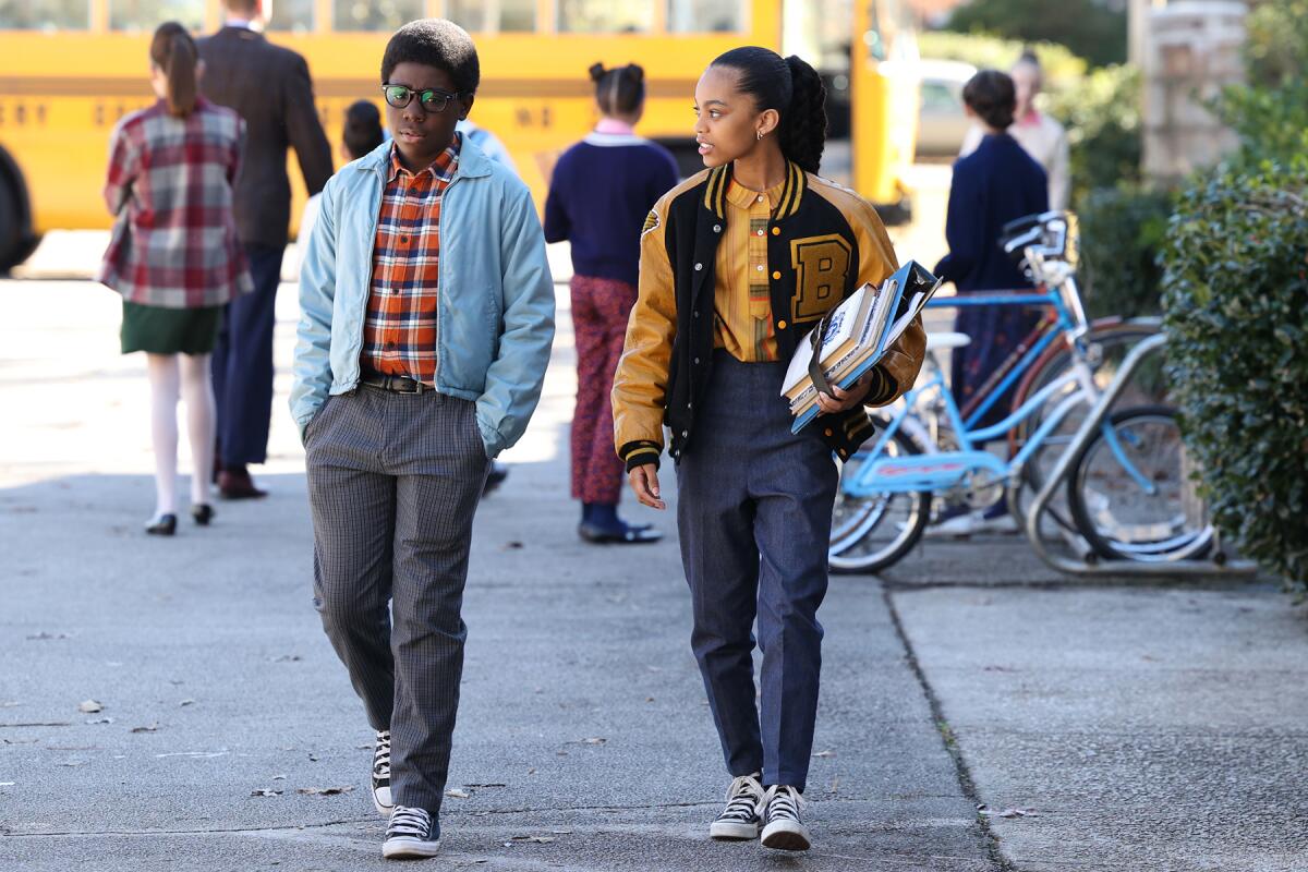 Two students walk side-by-side with a school bus in the background.