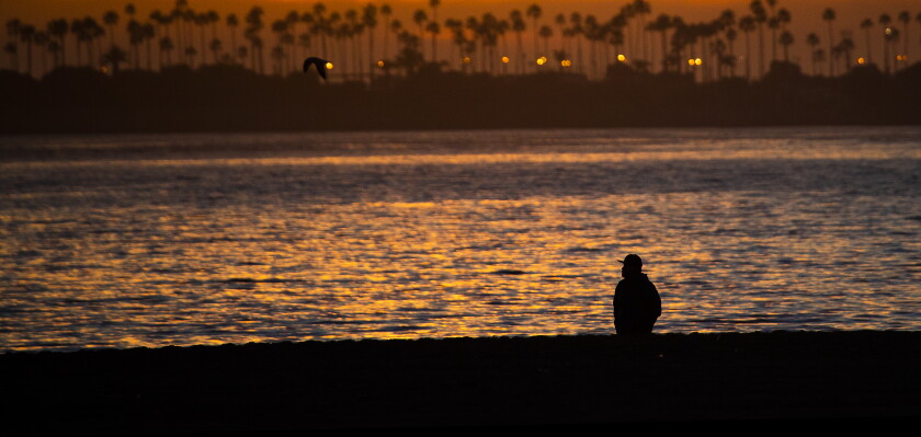 A beachcomber is silhouetted against the glowing sunset in Long Beach.