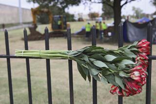 Flowers left by a mourner hang on a fence as crews work on a second test excavation and core sampling in the search for remains at Oaklawn Cemetery from the 1921 Tulsa Race Massacre Wednesday, Oct. 21, 2020. (Mike Simons/Tulsa World via AP)