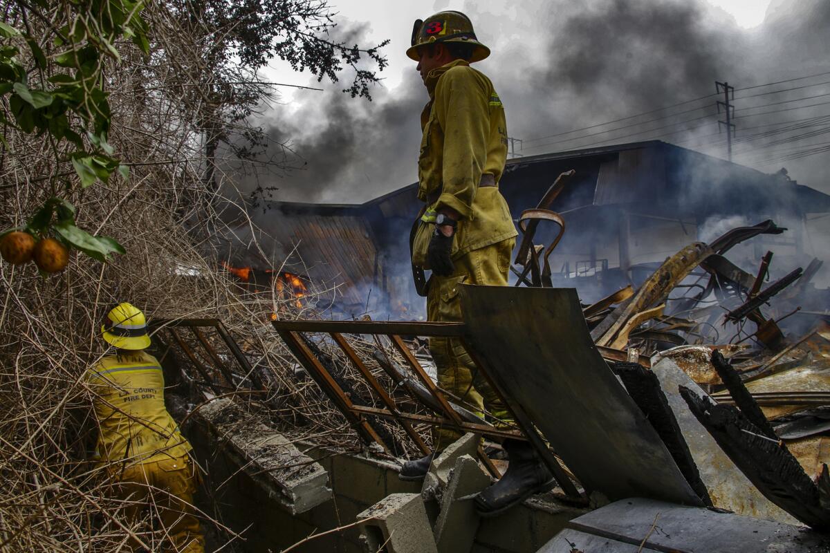 Los Angeles County firefighters clear brush at a residence in the 3500 block of 52nd Street to fight the fire from the back of a smoldering Maywood warehouse.