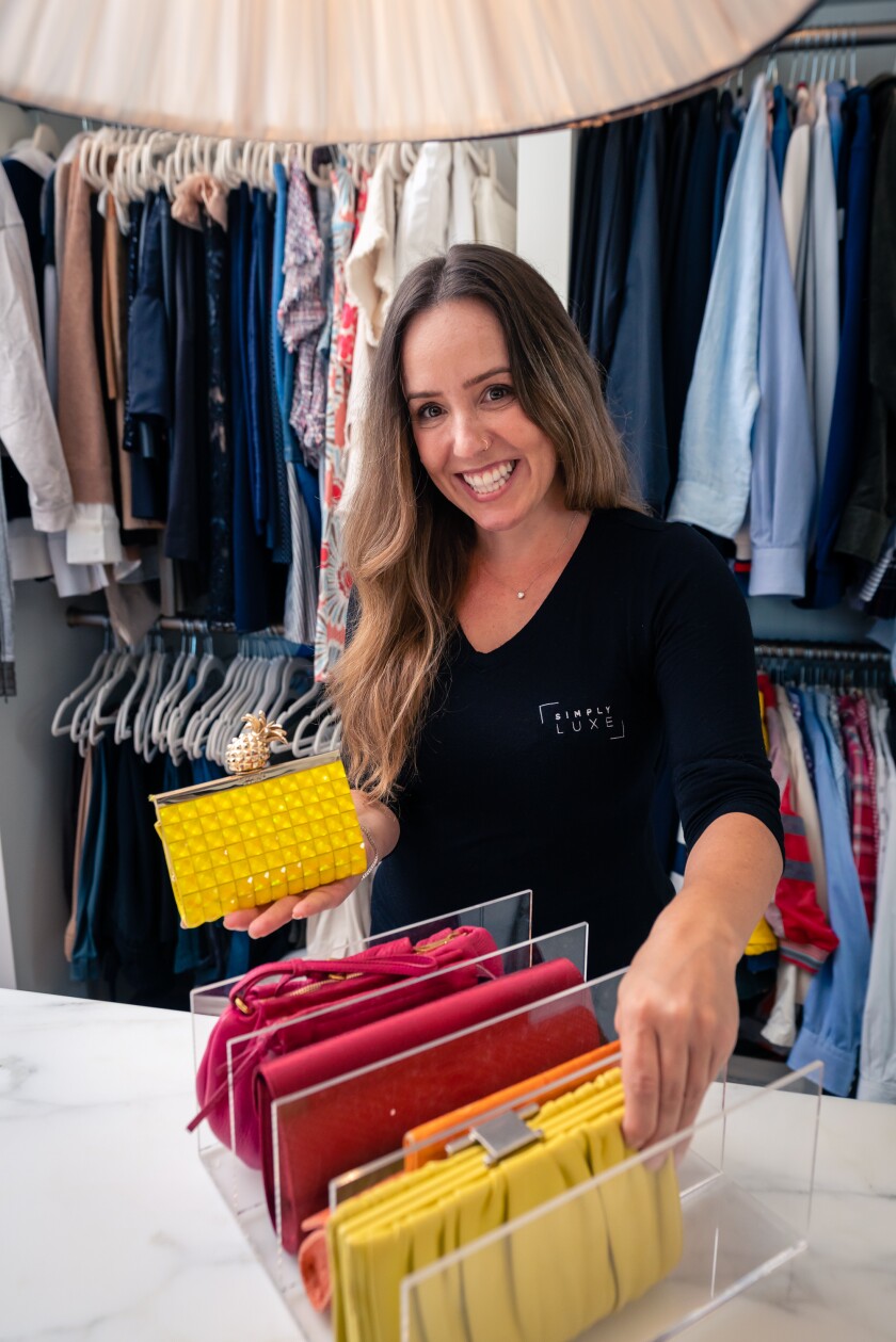 A professional organizer stands by an organized closet with a grouping of colorful handbags separated by clear dividers.