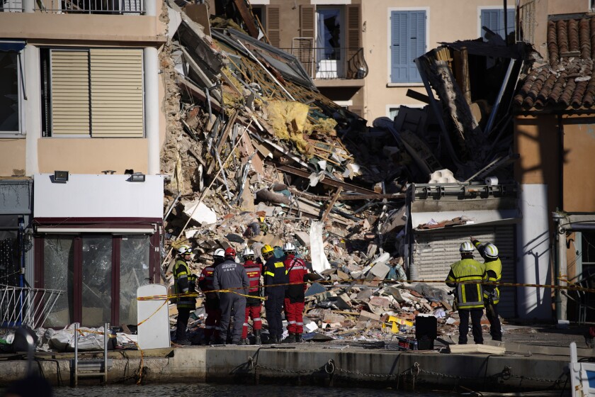Firemen and rescue workers stand at a three-story apartment building after it collapsed in a suspected gas explosion on southern France's Mediterranean coast, Tuesday, Dec. 7, 2021 in Sanary-sur-Mer. French rescue workers dug out the body of a man but also pulled a toddler and the child's mother alive from the rubble of the building that collapsed in a suspected gas explosion. Two other people are missing. (AP Photo/Daniel Cole)