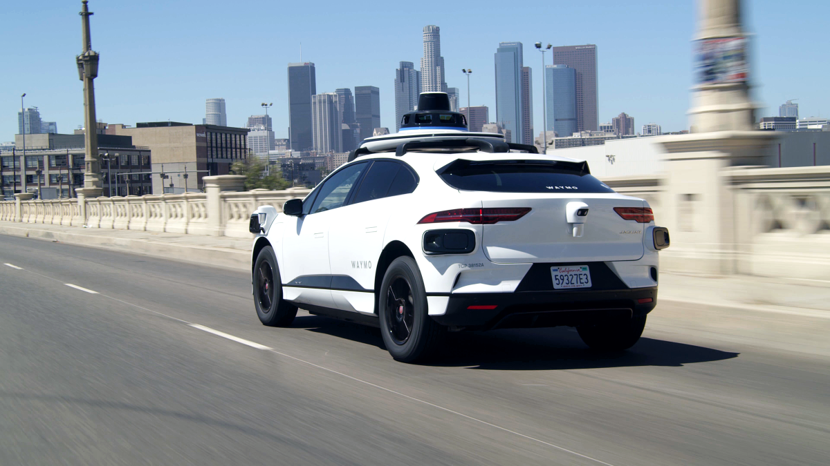 A white electric Jaguar I-Pace outfitted with Waymo full self-driving technology in Los Angeles.