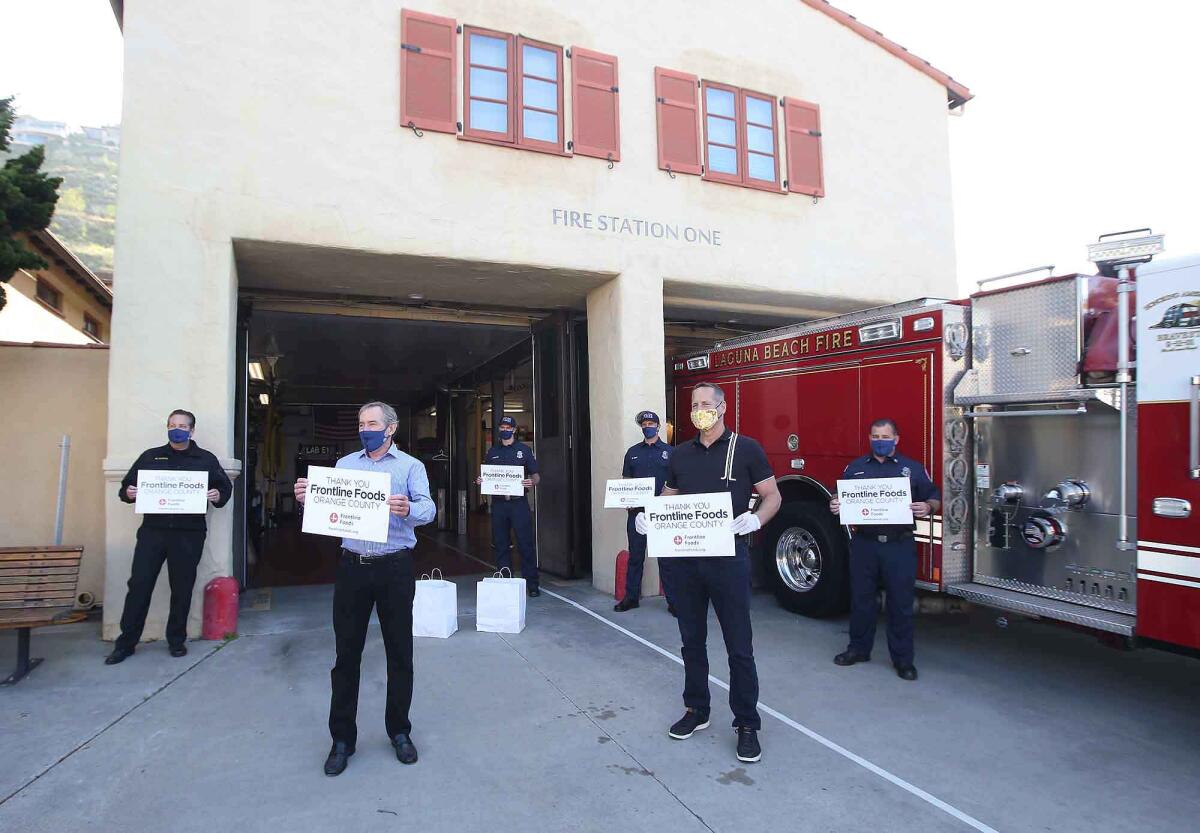 Laguna Beach Fire Chief Michael Garcia, Mayor Bob Whalen and Rep. Harley Rouda (D-Laguna Beach), from left and in front, and firefighters thank Frontline Foods with a group photo after they were given prepared meals on Monday.