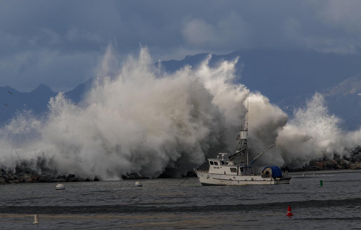 A giant wave crashes over a jetty as a fishing boat floats in the foreground.
