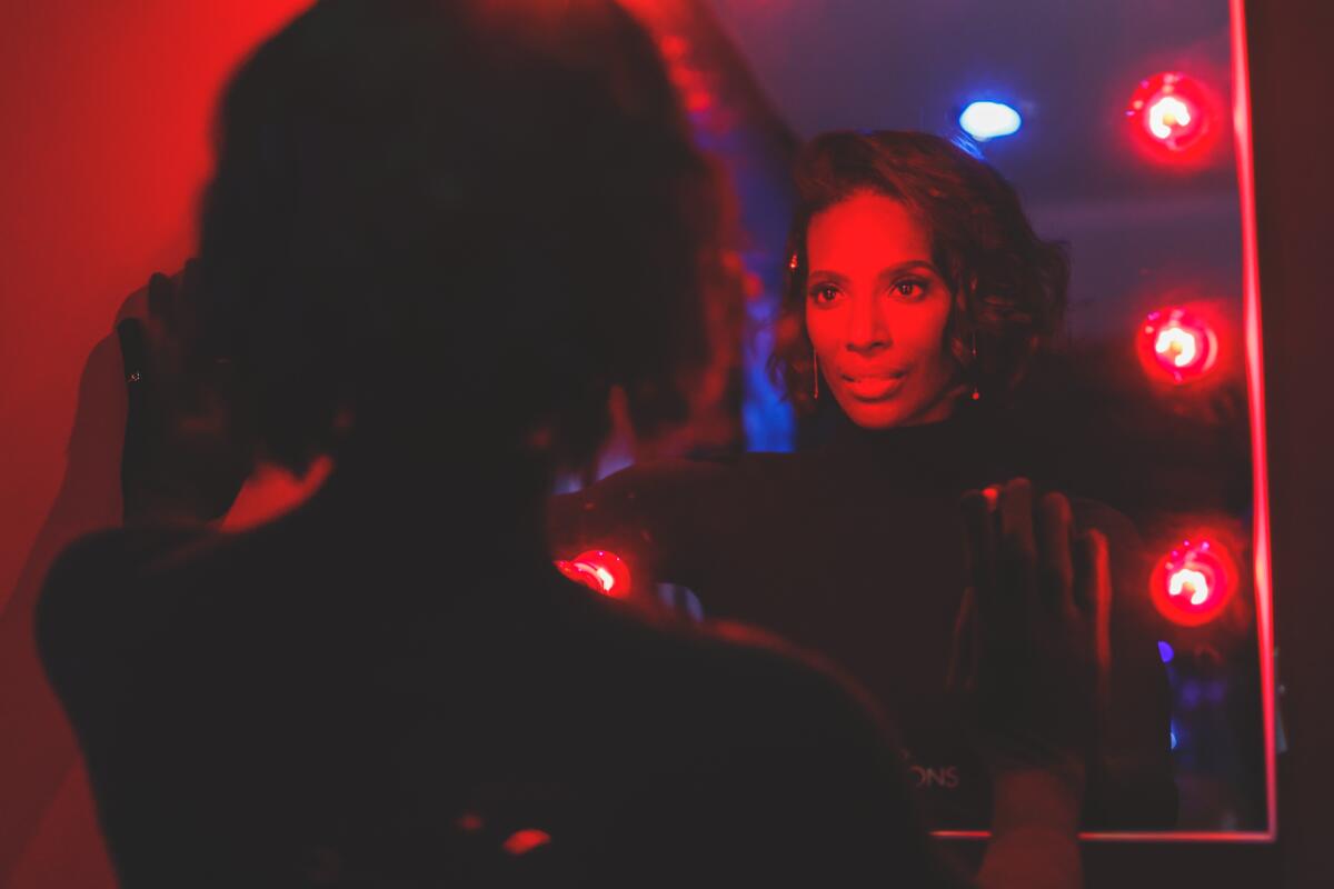 Woman dressed in black looking at her reflection in a mirror with red lighting
