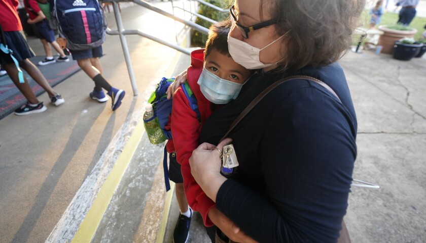 Maksim Mongayt, 7, hugs his mother Alexandra Mongayt in front of his elementary school on the first day of classes in Richardson, Texas, Tuesday, Aug. 17, 2021. Despite Texas Gov Greg Abbott's executive order banning mask mandates by local officials, the Richardson Independent School District and many others across the state are requiring masks for students. (AP Photo/LM Otero)