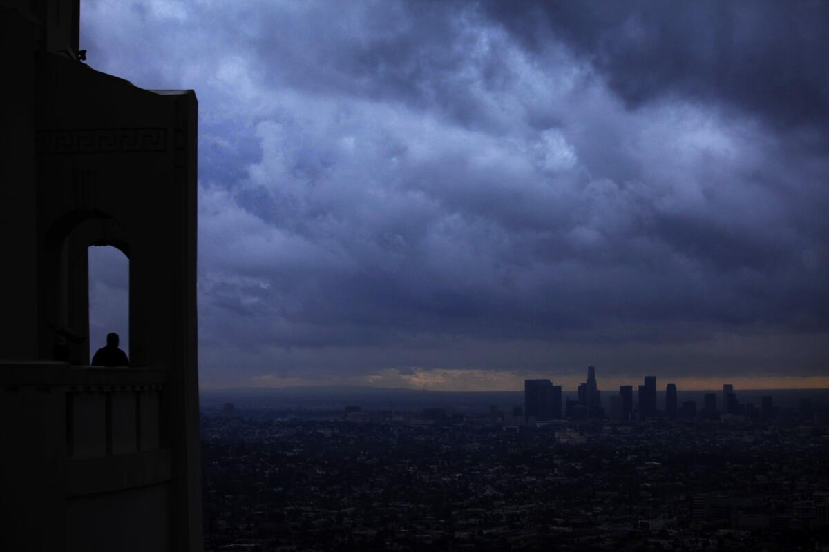A lone visitor to the Griffith Observatory watches as a storm front passes over downtown Los Angeles on Nov. 30. In San Jose, people are preparing to rappel down the side of a hotel.