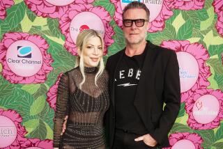 Tori Spelling, left, and Dean McDermott pose together against a floral background