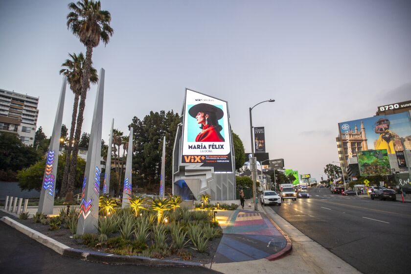 An irregularly shaped billboard on the Sunset Strip features a bright digital ad for Vix+ with Maria Felix.