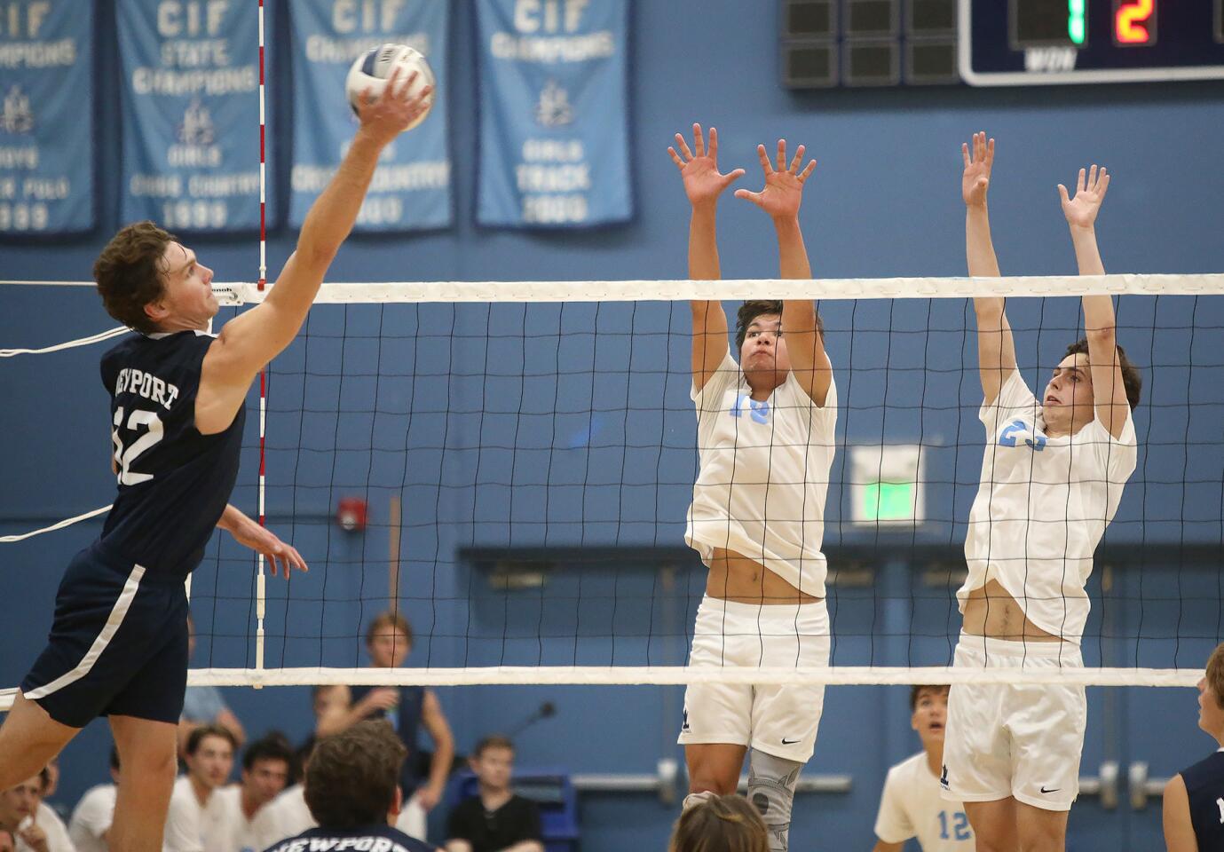 Newport Harbor's Dayne Chalmers, left, goes up high and wide to put the ball past two Corona del Mar blockers during second round of the Battle of the Bay boys' volleyball match in Surf League play on Wednesday.