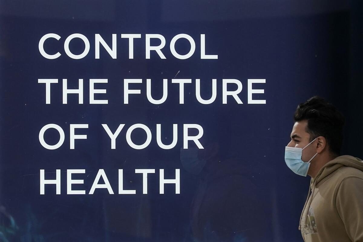 A pedestrian wears a face mask while walking past a sign at a Forward healthcare location during the coronavirus pandemic in San Francisco, Wednesday, Dec. 30, 2020. (AP Photo/Jeff Chiu)