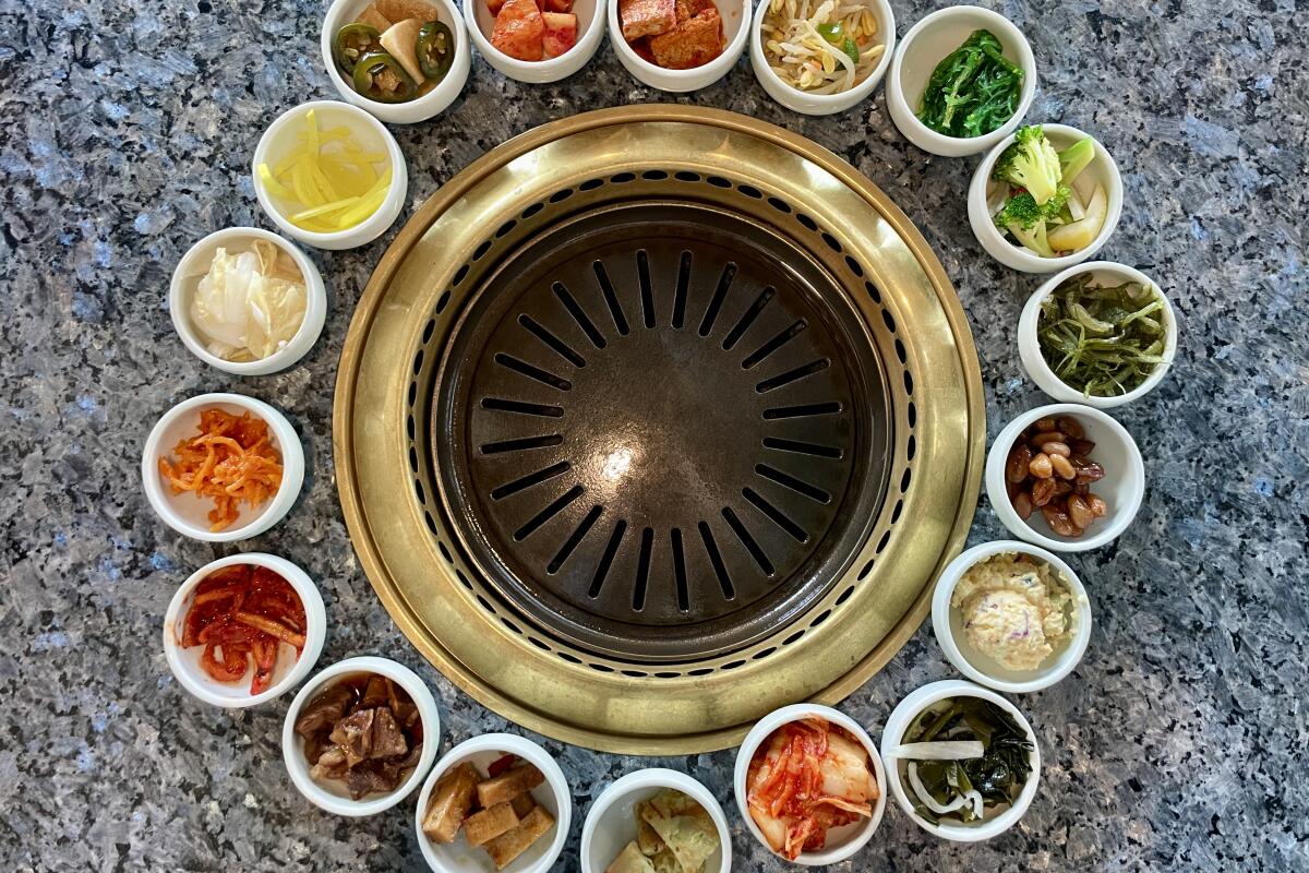 A selection of banchan surrounds a round metal grill at Genwa in Mid-Wilshire.