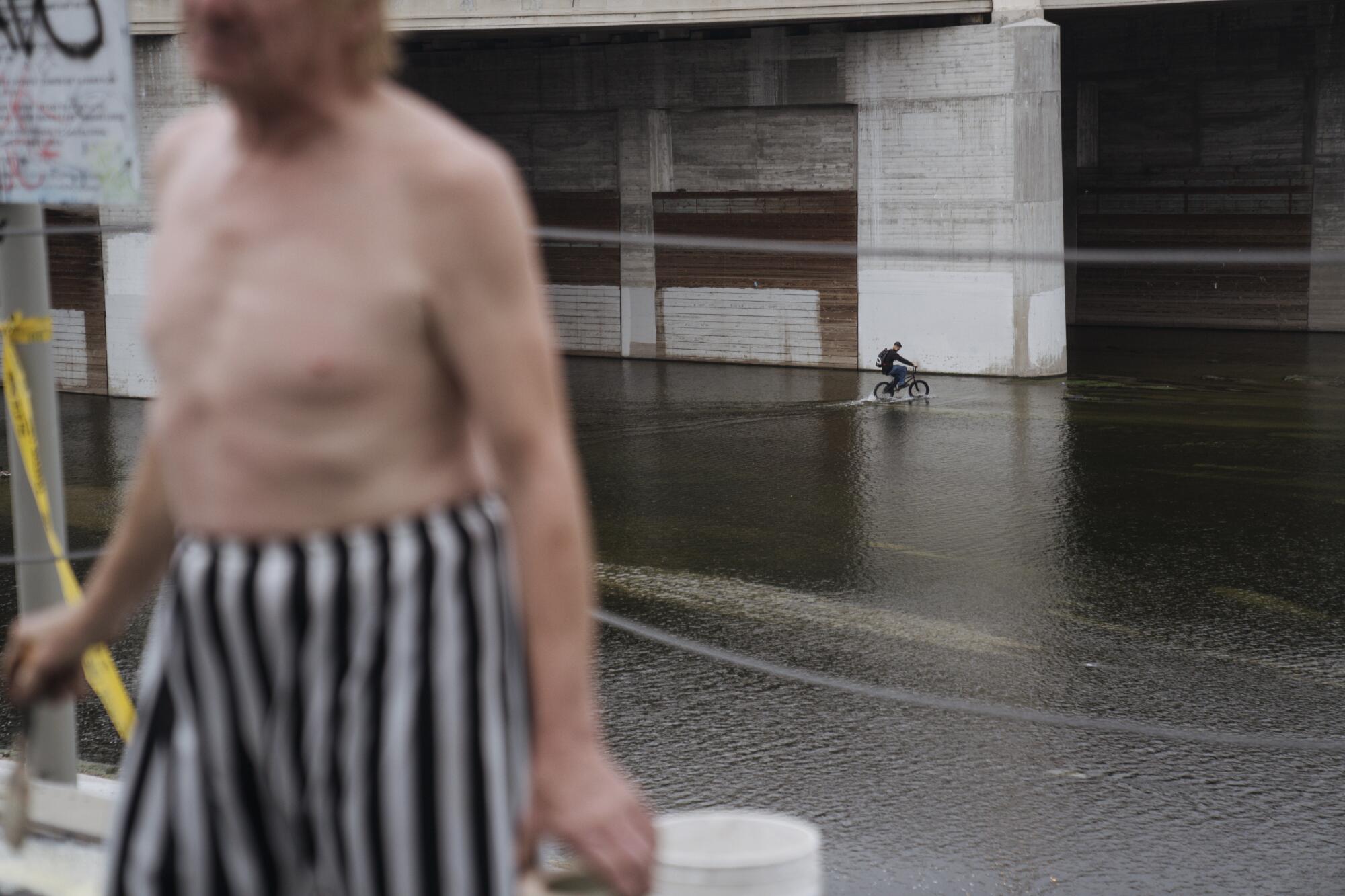 A shirtless man in striped shorts walks along the Los Angles River.