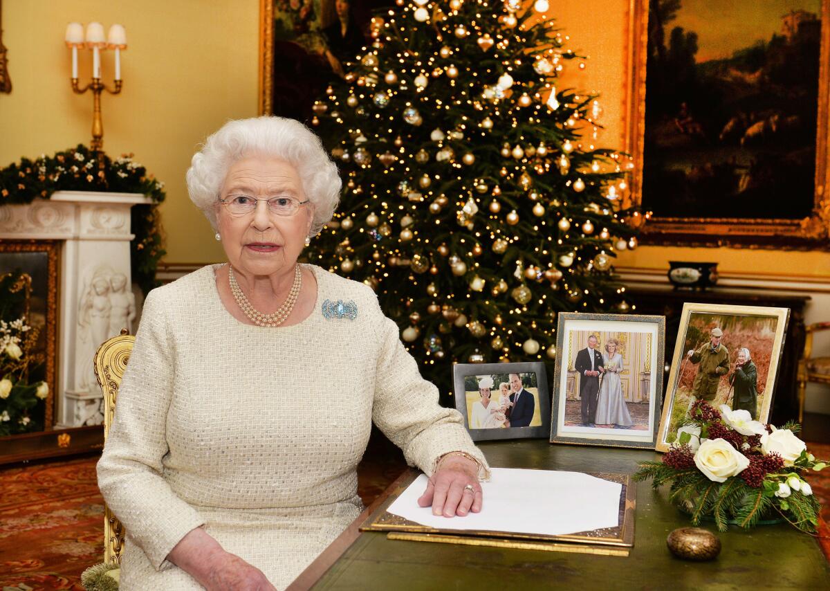 En esta imagen del 10 de diciembre de 2015, la reina Isabel II de Inglaterra en un escritorio en el palacio de Buckingham, en Londres, tras grabar su mensaje de Navidad a la Commonwealth, que se emitiría el viernes 25 de diciembre de 2015. En el escritorio se ven fotografías de la familia real. De izquierda a derecha, la reina con su marido el duque de Edimburgo; el príncipe Carlos con su esposa Camila, duquesa de Cornualles; y el príncipe Guillermo con su esposa Catalina y sus hijos, el príncipe Jorge y la princesa Carlota. (John Stillwell/Pool Foto via AP)