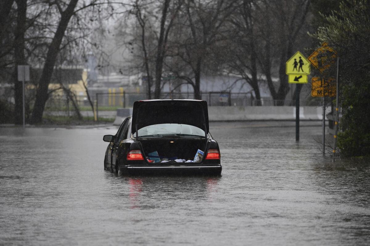 A car with a popped trunk sits in water up over its tires.