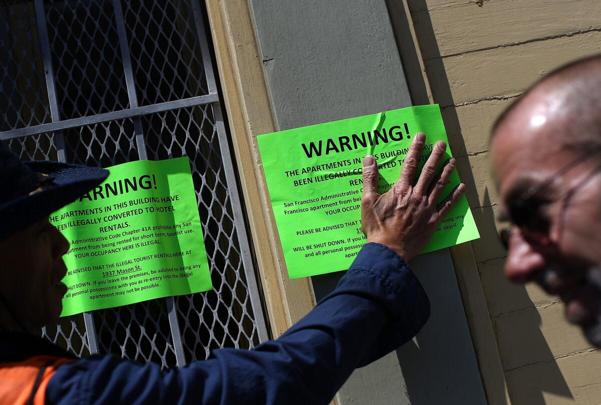 A protester with the San Francisco Tenant Union, seen in 2014, hangs a sign on the exterior of a city building that allegedly evicted all of the tenants so that the units could be converted to Airbnb rentals.