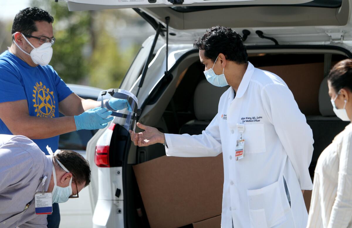 Dr. William Wang, center, chief medical officer at Dignity Health Glendale Memorial Hospital, looks over face shields delivered by Glendale Sunrise Rotary president Alex Parajon, left, and other members of the club, to the hospital on Tuesday.