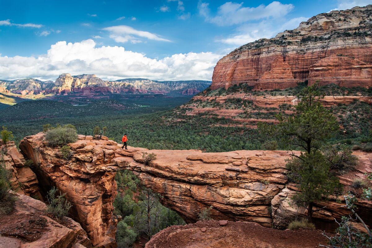 A distant view of a man walking across Devil's Bridge in Sedona, Arizona, with red rock hills nearby