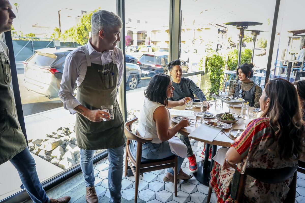 Server Miguel Diaz goes over the menu with customers at Fort Oak Restaurant where surcharges are levied on diners' bills.