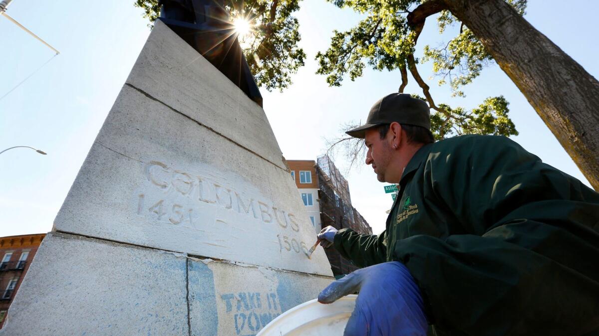 A statue of Christopher Columbus was marked with graffiti in Columbus Triangle park in Queens, N.Y., overnight. An employee of the New York Parks Department works to remove the writing, which said, "Tear it down. Don't Honor Genocide."