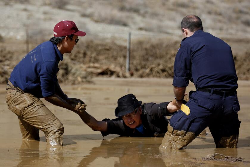 Photographer Travis Geske, left, and California Highway Patrol Officer Edward Stewart rescue TV cameraman Monte Duarte, who was sinking in the mud during a mudslide caused by heavy rains on California 58 east of Tehachapi on Oct. 16.