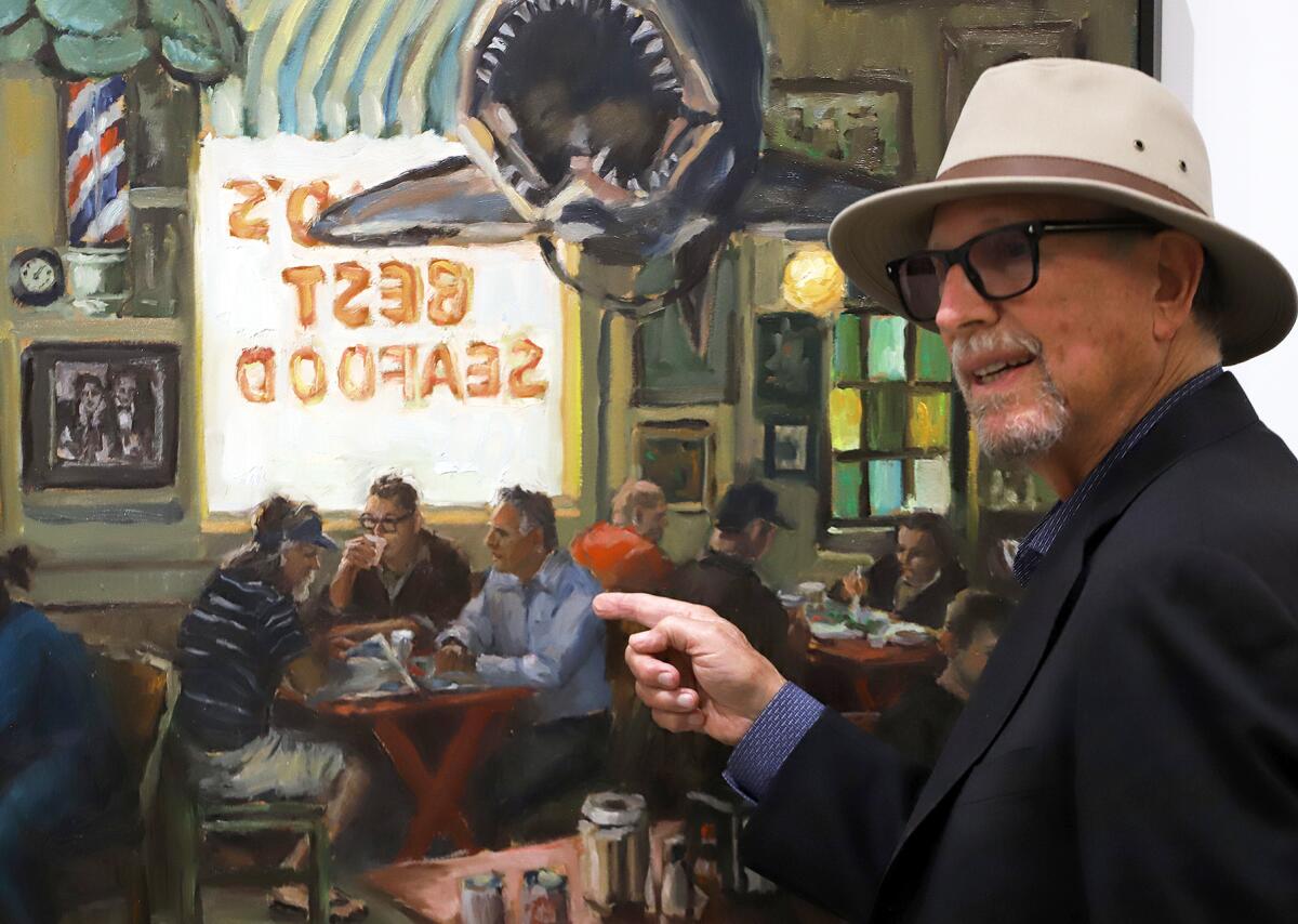 Mark Hilbert points to an oil painting by Bradford J. Salamon that depicts Hilbert dining at the Crab Cooker with two others.