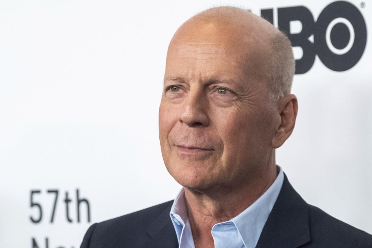 A close-up of Bruce Willis smiling. A backdrop says "HBO."