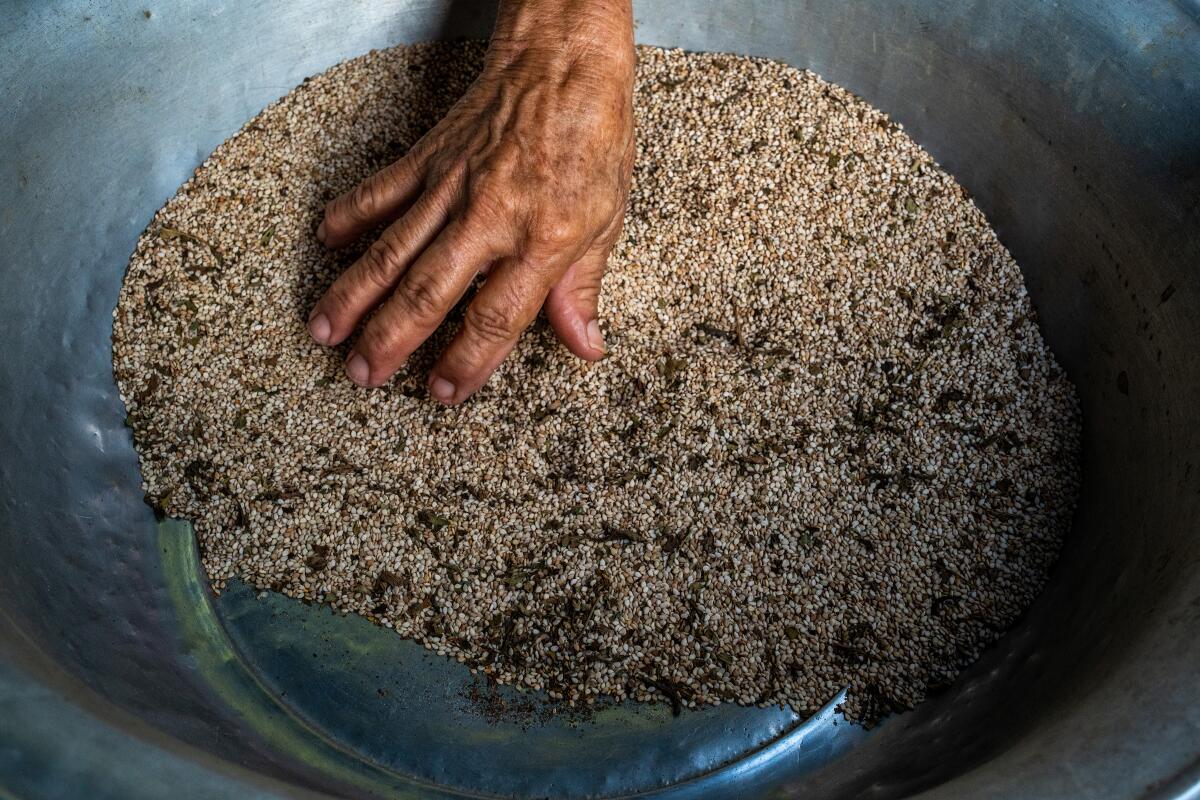 Sesame seeds being used to make hand-ground ajonjolí paste, in a bowl.
