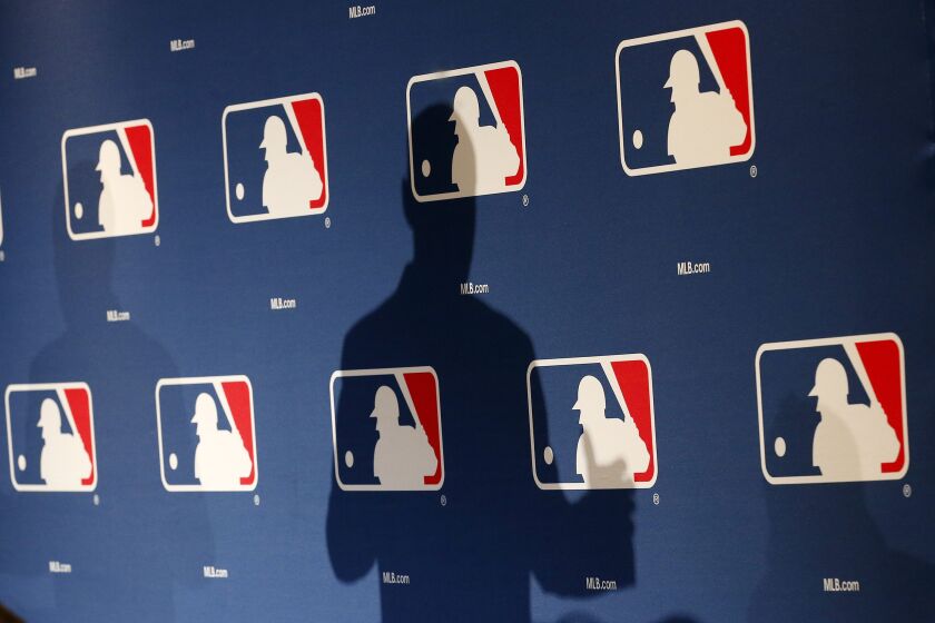 FILE - In this Monday, Feb. 23, 2015 file photo, the shadow of MLB Commissioner Rob Manfred is projected on an MLB logo backdrop in Phoenix. Major league teams steeply increased the money spent on young players in 2015, but the overall percentage of revenue devoted to players has remained relatively stable for a decade. (AP Photo/Ross D. Franklin)