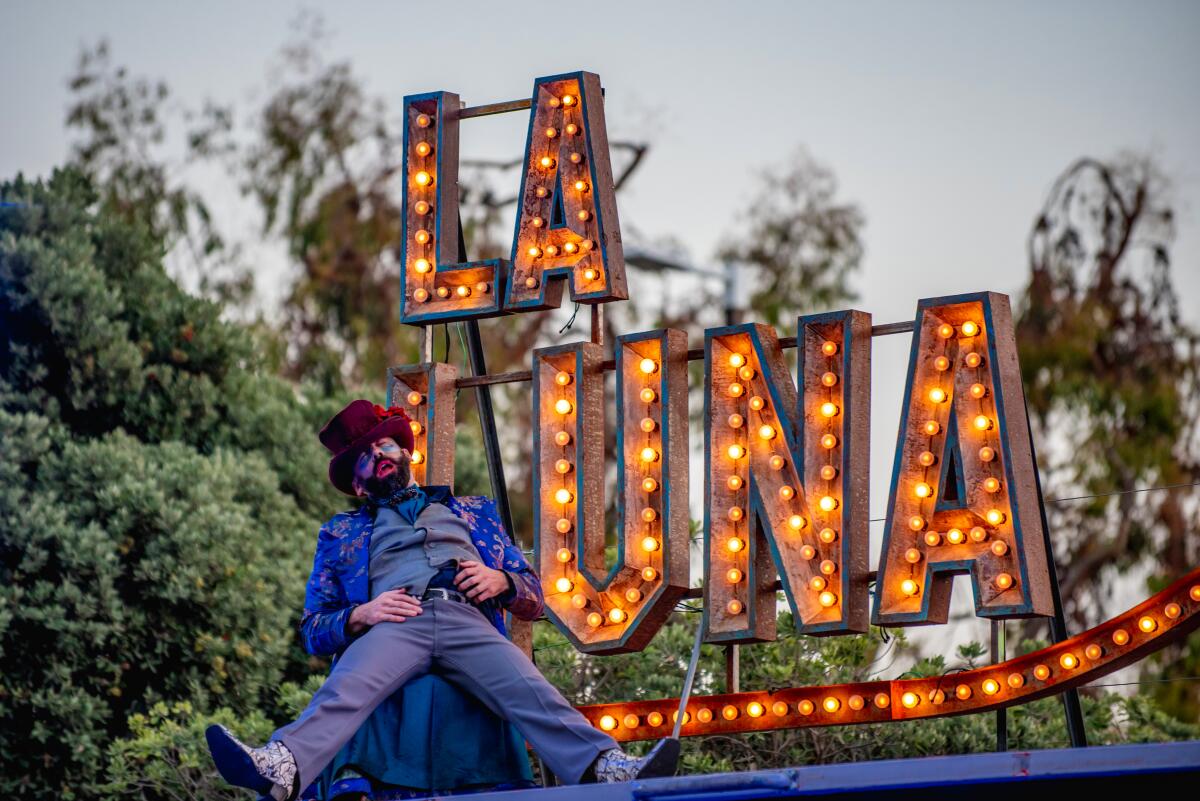 A man in a purple suit and red top hat sits back before an illuminated sign that reads "La Luna"