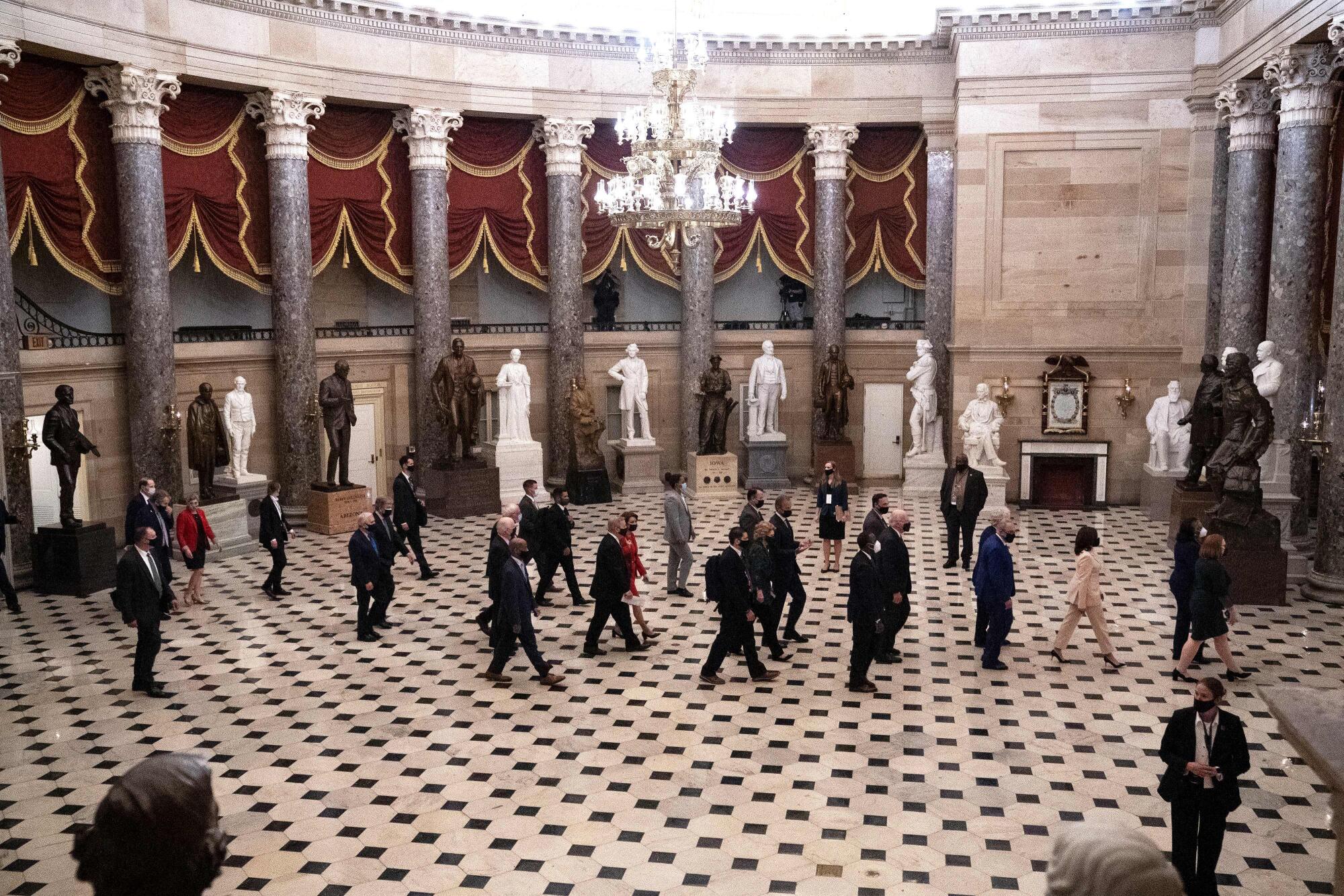 A line of people walk across a hall.