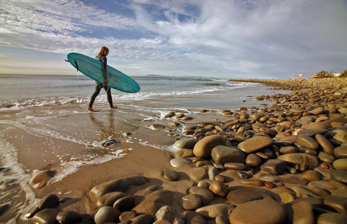 A surfer walks the beach in Santa Barbara. An ocean swell is expected to produce high surf Monday and Tuesday.
