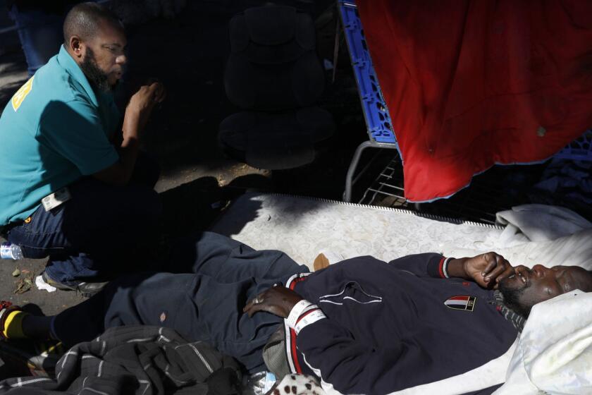 LOS ANGELES, CA MARCH 5, 2018: Geoffrey Goosby, Los Angeles Homeless Services Authority (LAHSA) worker with the Emergency Response Team Homeless Services Department, left, offers help to a man laying on a mattress on a sidewalk in south Los Angeles, CA March 5, 2018. The man refused help and refused to be taken to the hospital via ambulance. He still had his hospital bracelet on his wrist. Under the current law, he has the right to refuse care. (Francine Orr/ Los Angeles Times)