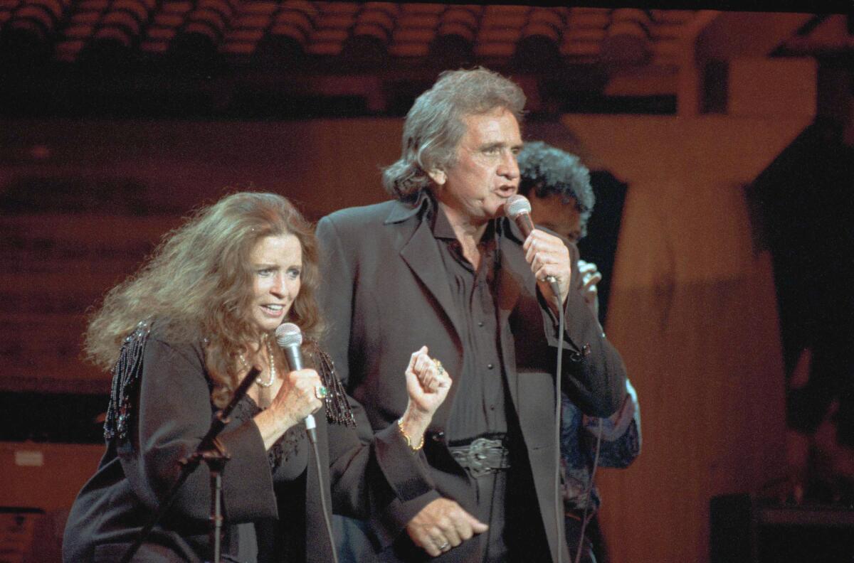 A man and a woman, both dressed in black, sing into microphones on stage.