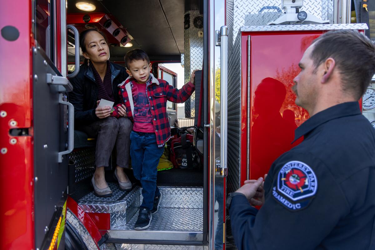 May Tom and her son inside a firetruck, with firefighter David Lawson nearby.