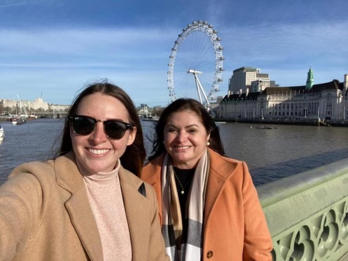Two women pose for a selfie on a bridge with a Ferris wheel in the background.