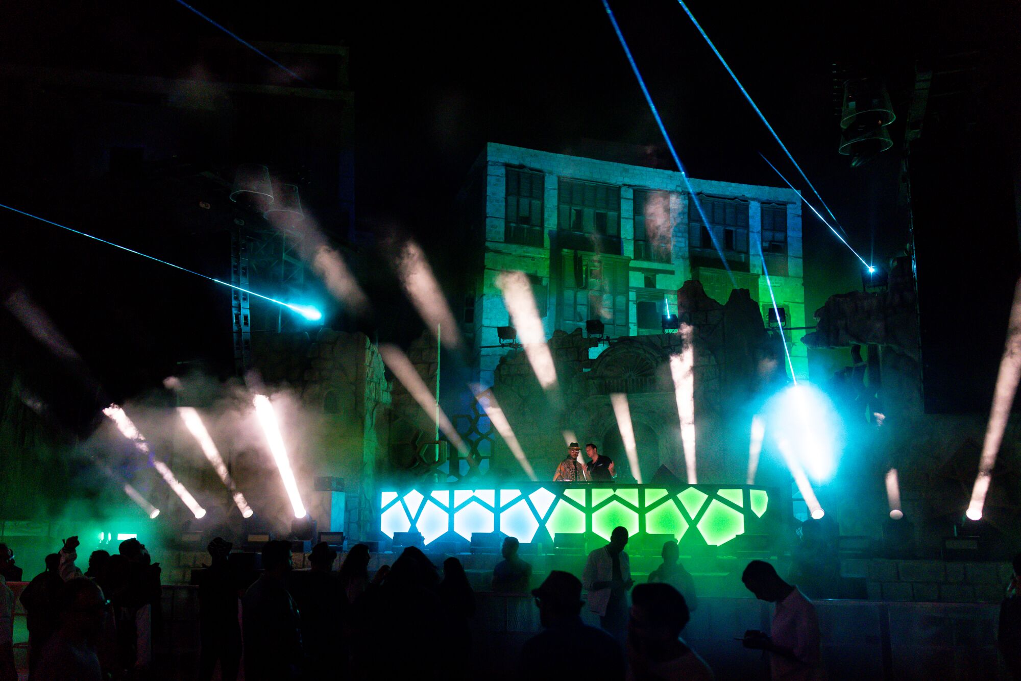 Light show on a green and blue stage at a night rave.