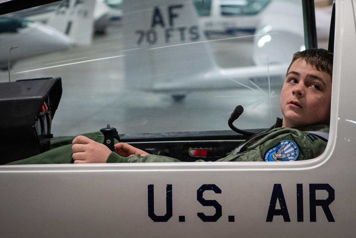 A boy sitting in a fighter jet cockpit.