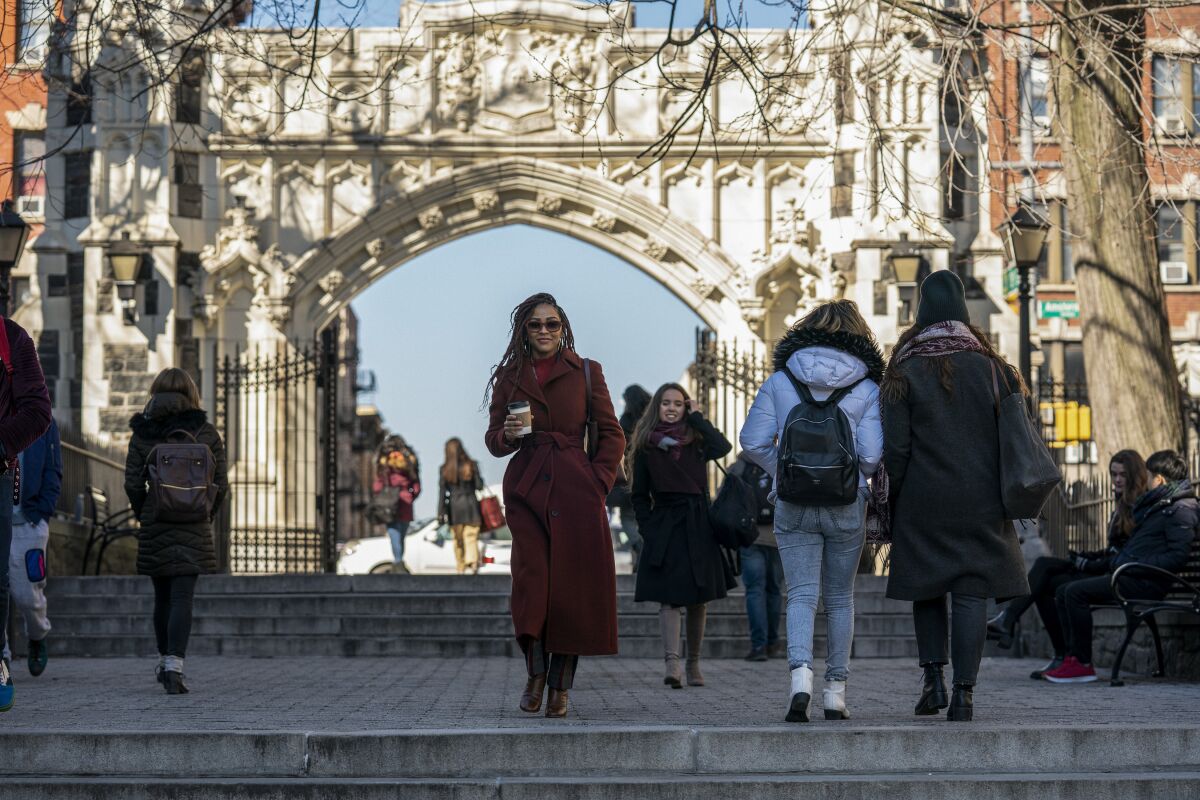 A woman in a red count walking with a coffee at Columbia University
