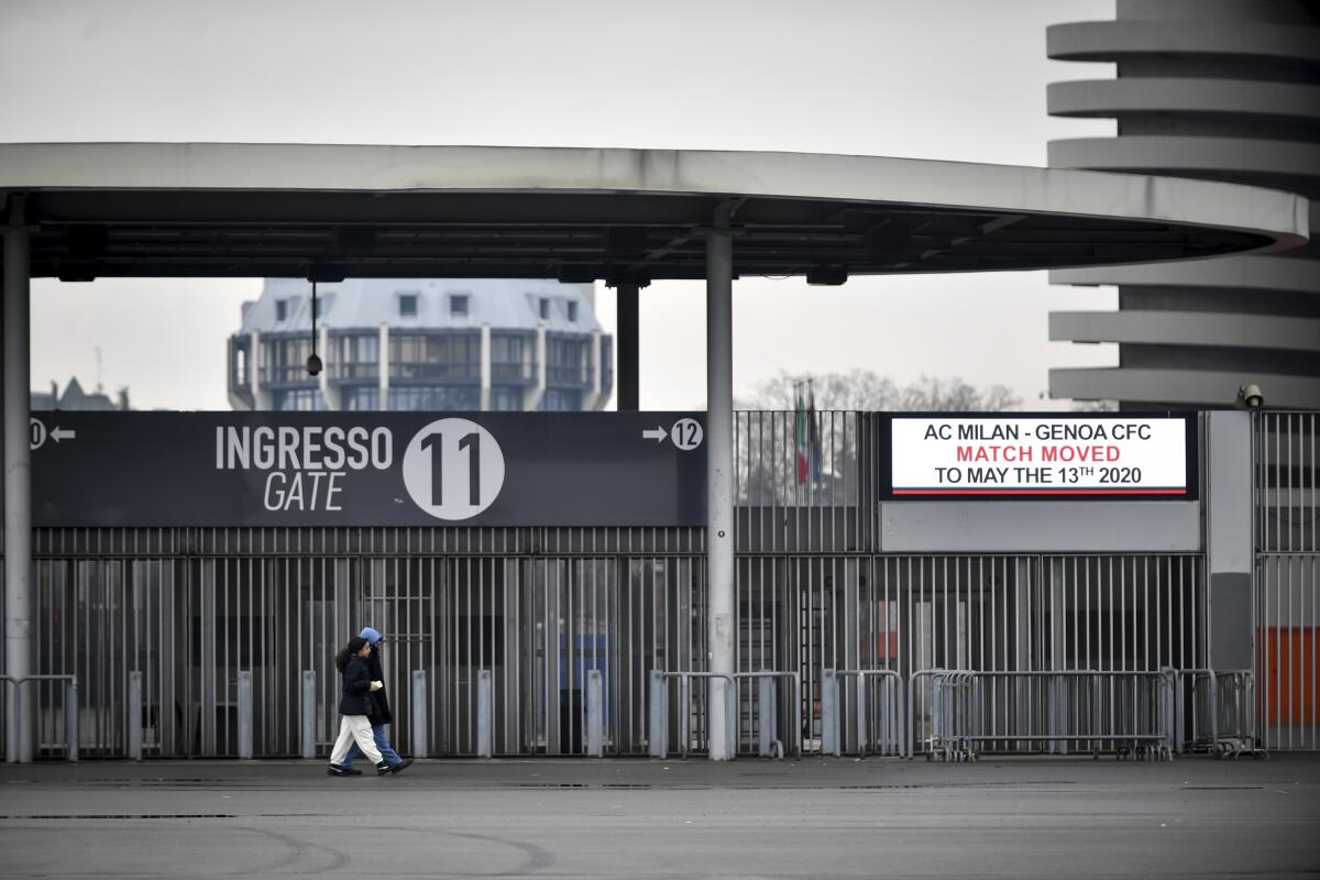 People walk outside San Siro stadium where a notice advising that the Serie A soccer match between AC Milan and Genoa is postponed to May 13, 2020, in Milan, Italy.