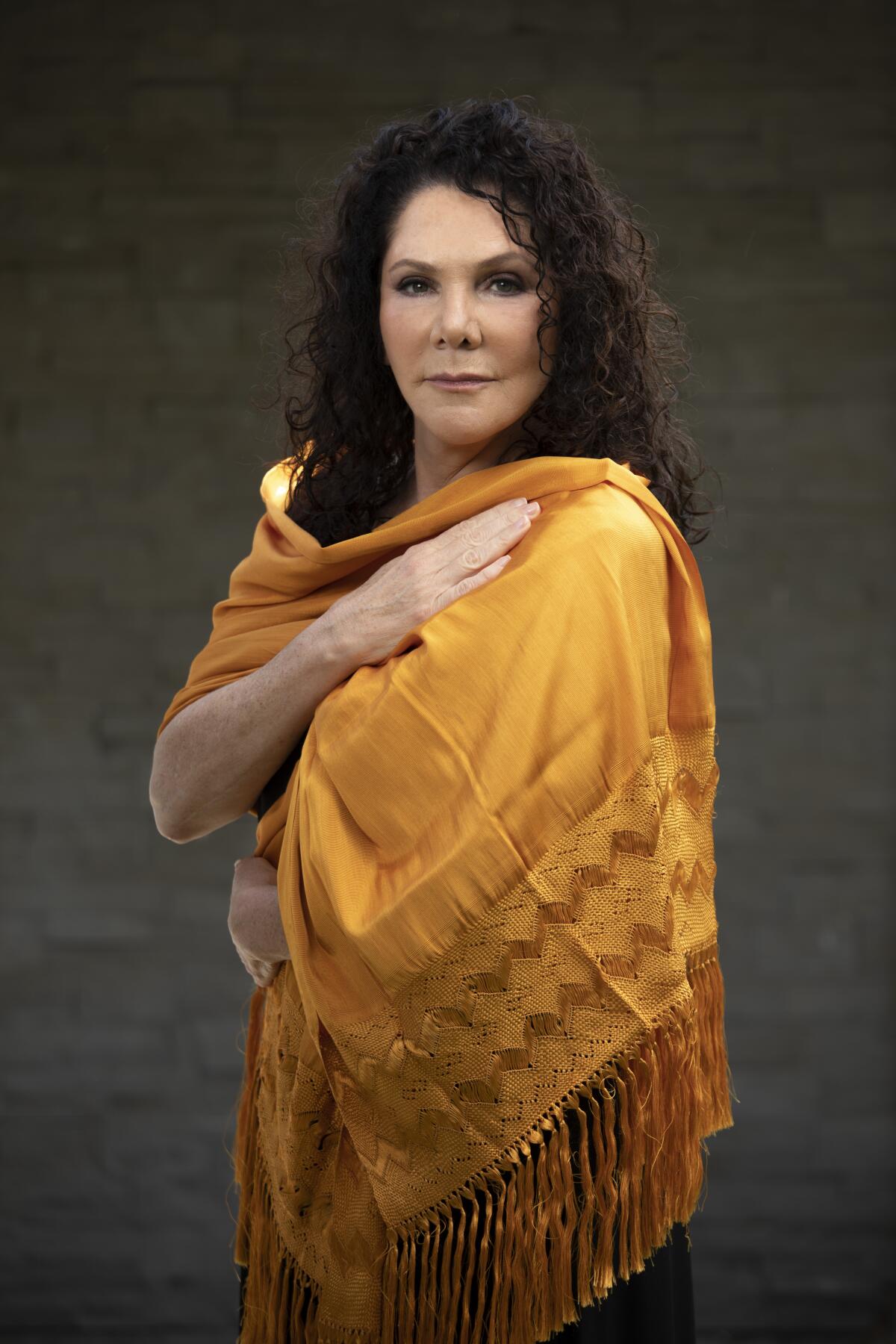 Author Maria Amparo Escandón stands wrapped in a gold shawl.